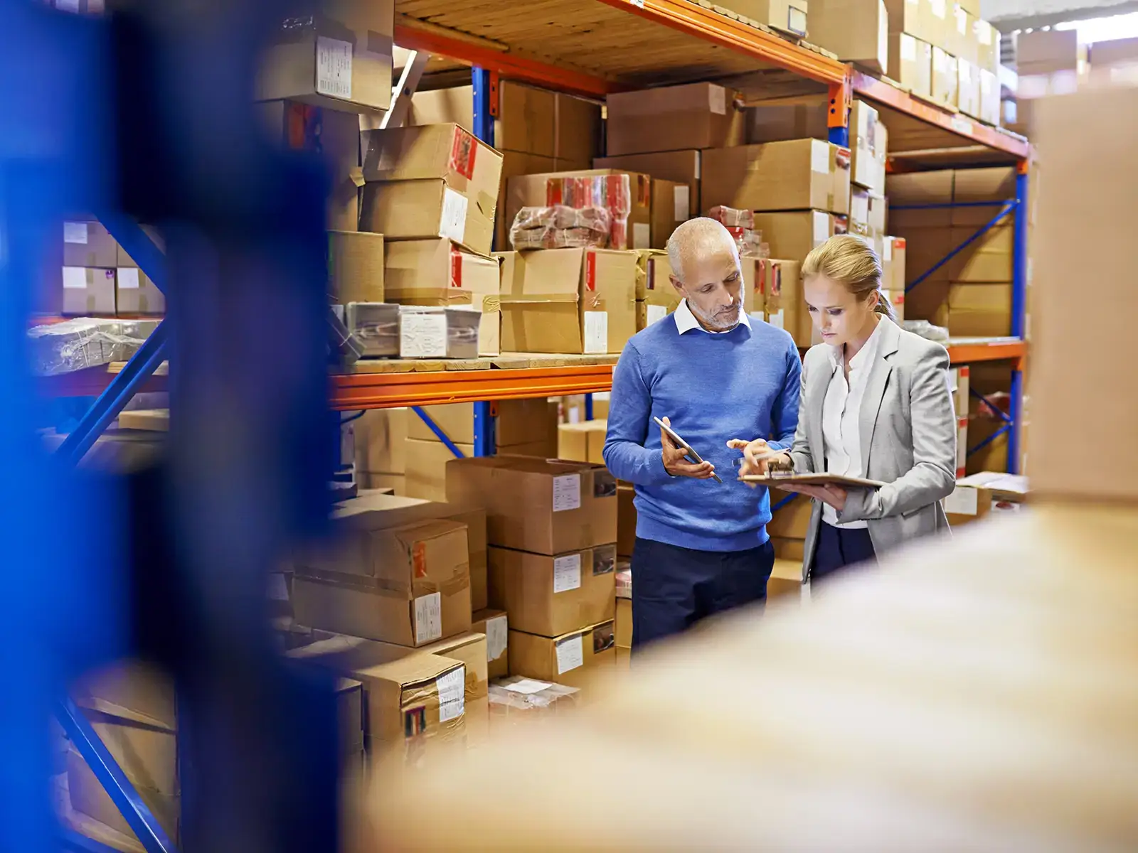 Twee collega’s in een magazijn die samen voorraad controleren op tablets en notitieblok, symbool voor samenwerking en kennisdeling.