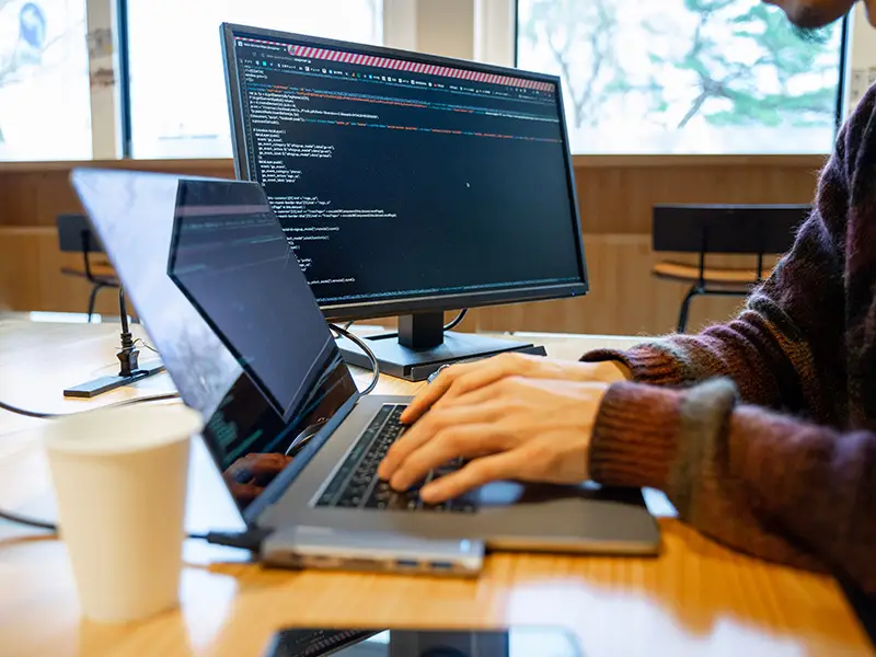Ontwikkelaar bouwt en test webshopcode op laptop en tweede scherm – retailZ helpt MKB met schaalbare webshopontwikkeling.